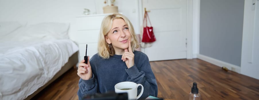 Portrait of young charismatic woman, girl records video while putting on makeup, reviewing beauty products for social media account, has a lifestyle blog, holding mascara.