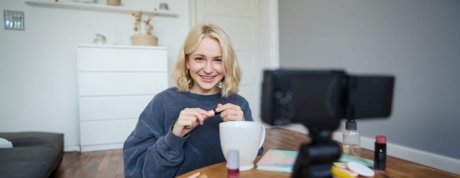 Portrait of blond smiling woman records a lifestyle blog, vlogger or makeup artist recording video for social media, holding mascara, reviewing beauty products for followers online.