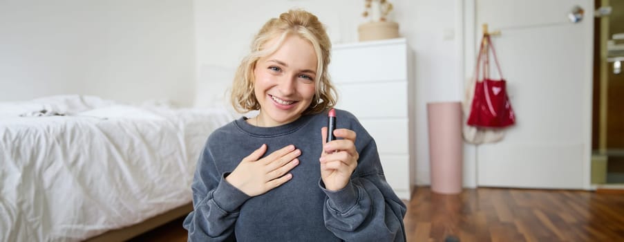 Portrait of young beautiful woman, content maker creating a new vlog, beauty video, showing lipstick, recommending makeup, records a tutorial.