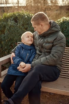 Autumnal Family Affection: Father, 40 Years Old, and Son - Beautiful 8-Year-Old Boy, Seated in the Park. Embrace the warmth of familial love in the autumnal air with this heartwarming image. A father, 40 years old, and his son - a beautiful 8-year-old boy, seated in the park. The essence of autumn adds a touch of seasonal charm to this delightful moment of family affection.