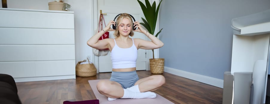 Portrait of fit and healthy young woman in wireless headphones, does workout, using online video tutorials, listens to fitness instructor on laptop, exercising at home.