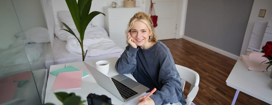 Portrait of young woman distance learning, working from home with laptop, making notes, student studying on remote, doing online course.