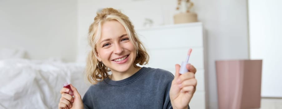 Close up portrait of woman recording a video of herself, holding beauty product, recommending lip gloss, content maker advertising makeup on her blog, smiling at camera.