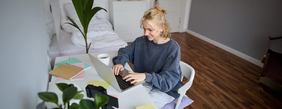 Portrait of young woman distance learning, working from home with laptop, making notes, student studying on remote, doing online course.