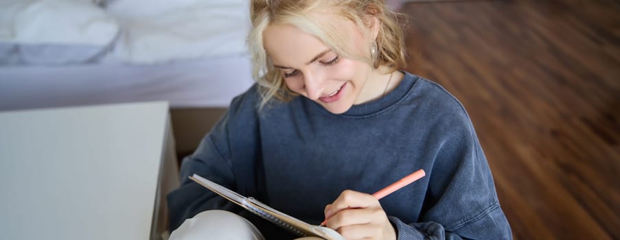 Close up portrait of smiling girl, writing in notebook, adds notes to her diary, smiling while doing homework.