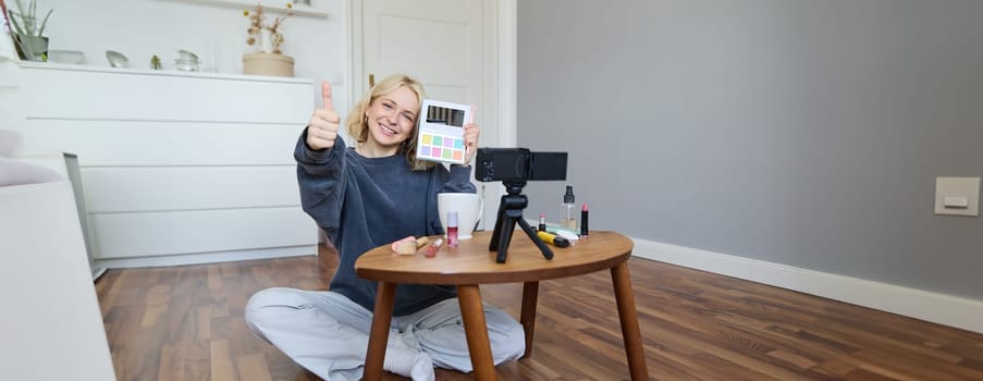 Portrait of beautiful smiling woman, recording video in her room, has camera on coffee table, reviewing makeup, doing lifestyle vlog for social media account, records a tutorial.