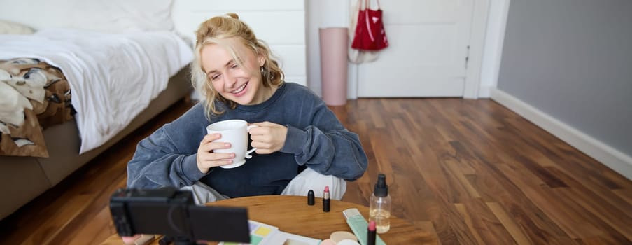 Portrait of young online influencer, social media blogger records new lifestyle video in her room, has digital camera connected to stabiliser, sitting in cosy space on floor, chatting about makeup.