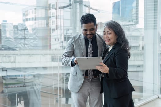 Two happy diverse coworker discussing report on tablet, working on project together.