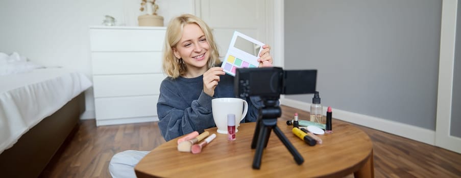 Portrait of beautiful smiling woman, recording video in her room, has camera on coffee table, reviewing makeup, doing lifestyle vlog for social media account, records a tutorial.