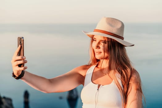 Selfie woman in hat, white tank top and shorts makes selfie shot mobile phone post photo social network outdoors on sea background beach people vacation lifestyle travel concept