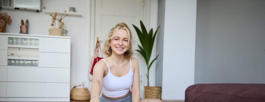 Vertical shot of smiling young woman, content creator using digital camera during workout, shooting a video vlog about fitness training and home exercises, recording her yoga.