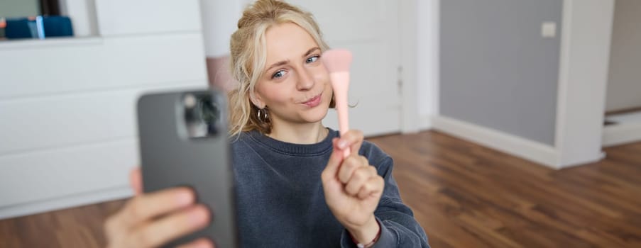 Portrait of young woman, girl beauty blogger, recording vlog in her bedroom, doing makeup tutorial for social media followers, taking selfies, live streaming on mobile phone app.