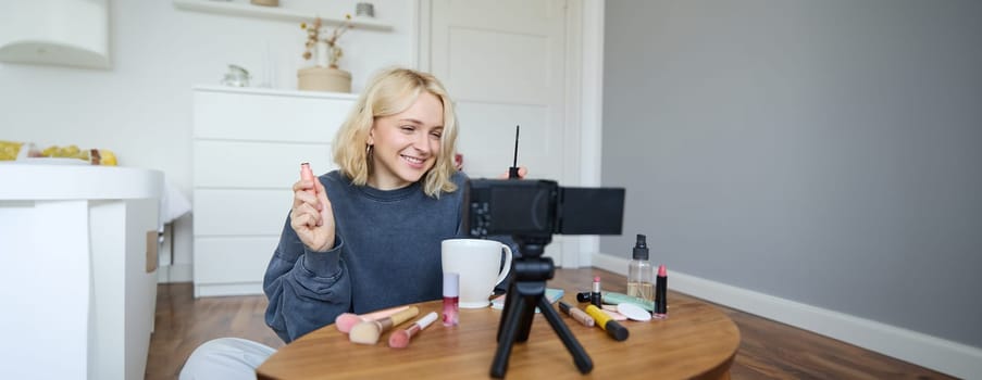 Portrait of blond smiling woman records a lifestyle blog, vlogger or makeup artist recording video for social media, holding mascara, reviewing beauty products for followers online.
