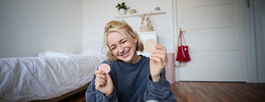 Portrait of happy, beautiful blond woman, showing makeup products on camera, recording vlog, social media content for followers, online live stream about beauty items.