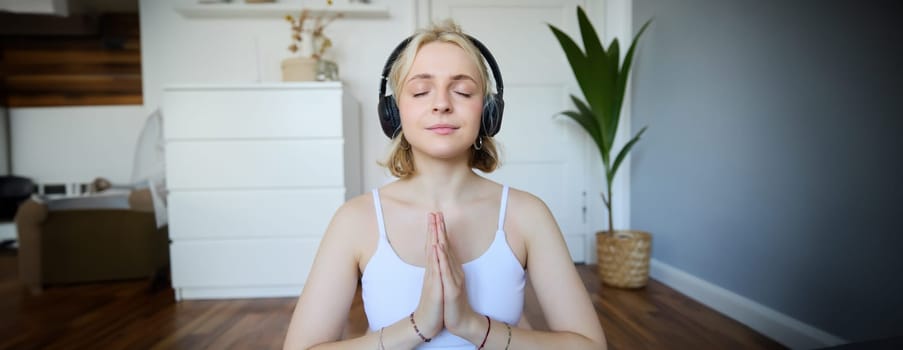 Wellbeing and people concept. Close up portrait of young woman in headphones, meditating, practice yoga, listens to podcast in earphones.