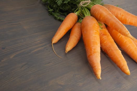 Bundle of vibrant orange carrots with green leafy tops is neatly tied together using twine and positioned on an old, rustic wooden table