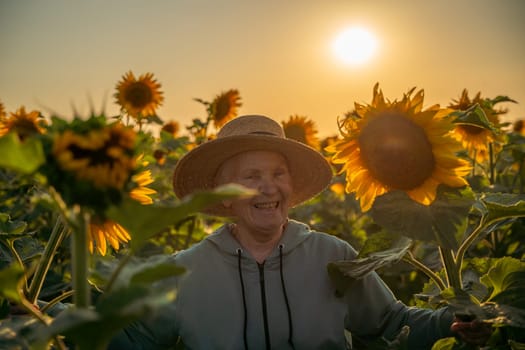A woman wearing a straw hat stands in a field of sunflowers. The sun is setting in the background, casting a warm glow over the scene. The woman is enjoying the beauty of the flowers