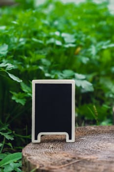 Blank Black billboard against green field garden fresh green herb parsley. Empty mockup template Blackboard label at farm land. Copy space banner for your text. Agricultural landscape advertisement sample