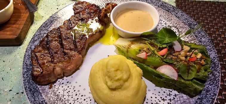 Beef New York strip loin steak or sirloin steak served with potatoes, and mushroom sauce and salad on plate Marble premium beef