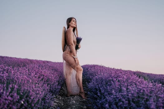 Close up portrait of young beautiful woman in a white dress and a hat is walking in the lavender field and smelling lavender bouquet.
