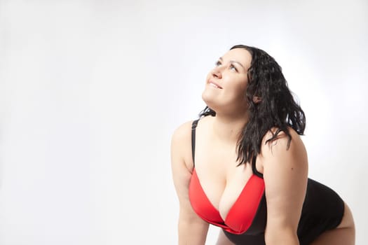 Portrait of attractive dreamy thick woman in red black swimsuit posing on white background. Body positive, photoshoot, selfie. Funny plus size model