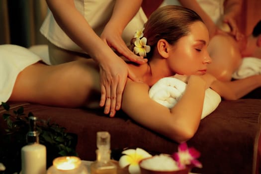 Caucasian couple customer enjoying relaxing anti-stress spa massage and pampering with beauty skin recreation leisure in warm candle lighting ambient salon spa at luxury resort or hotel. Quiescent