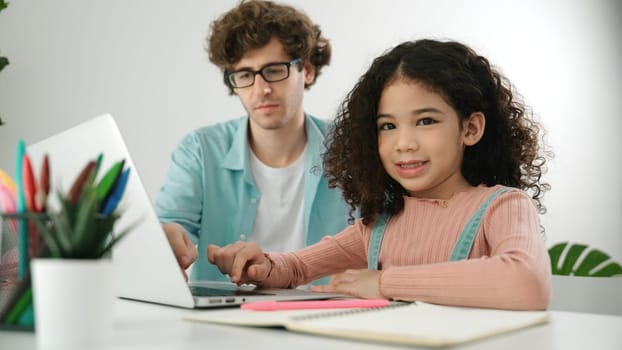 American student looking at camera while working on laptop with dad sitting and looking at laptop screen to check engineering code. Happy school girl smiling while study about generate ai. Pedagogy.