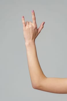 Female hand gesturing rock sign on gray background close up