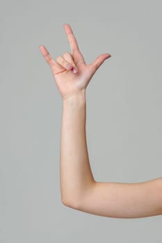 Female hand gesturing rock sign on gray background close up