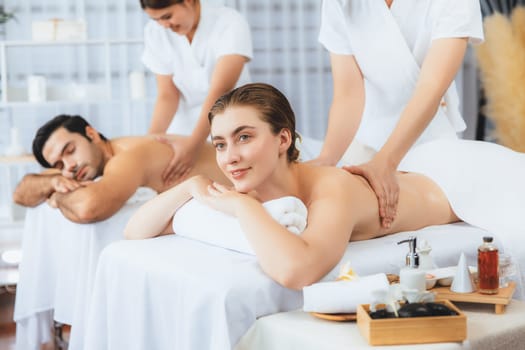 Caucasian couple customer enjoying relaxing anti-stress spa massage and pampering with beauty skin recreation leisure in day light ambient salon spa at luxury resort or hotel. Quiescent