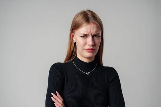 Young Woman In Black Shirt Expressing Discontent Against Grey Background close up