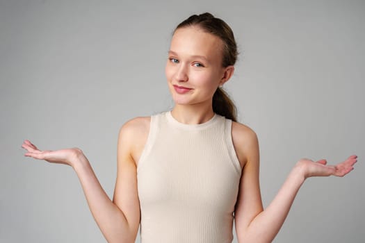 Young Clueless Woman Standing With Outstretched Arms on gray background in studio