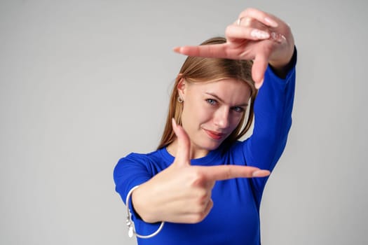 Young Woman in Blue Shirt Making Hand Sign on gray background in studio