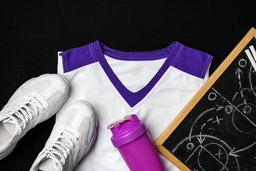 A pair of white sneakers, a white and purple sports jersey, a bright purple water bottle, and a blackboard with tactical diagrams are laid out, suggesting a preparation for a sports game or a strategy session.