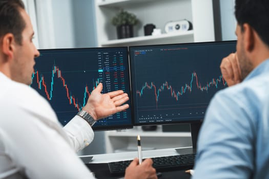 Stock traders discussing on research market stock database at real time by using two pc screen for comparing with the past of valued and current exchange analyzed business dynamic by minute. Sellable.