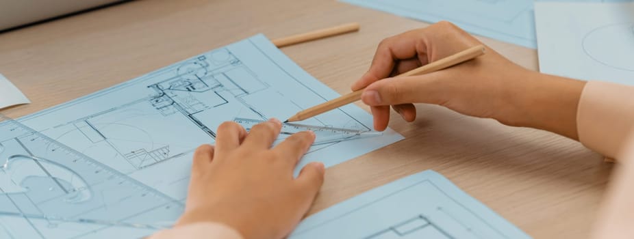 Professional architect hand drawing a blueprint by using ruler measuring length on table with architectural equipment and blue print scatter around at modern office. Closeup. Delineation.