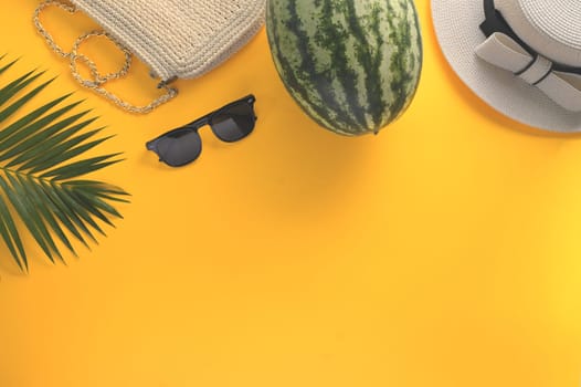 Straw hat, sunglasses, watermelon and palm leaf on yellow background. Summer and travel vacation concept.