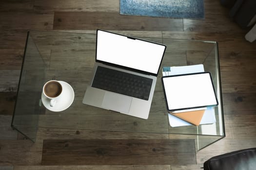 Top view laptop with blank screen, digital tablet, document and coffee cup on glass table in living room.