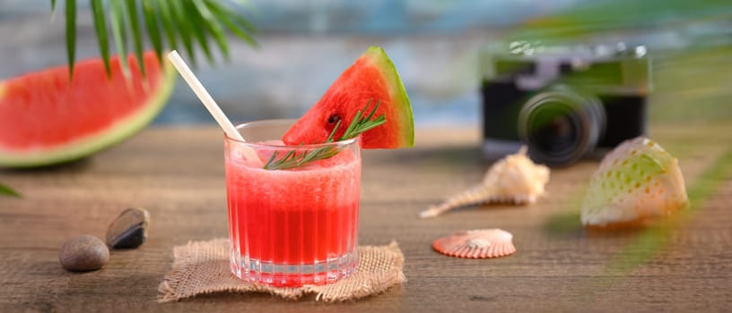 Fresh watermelon juice, seashells and camera on wooden table. Summer vacation and travel concept.