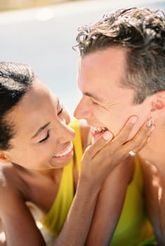 Laughing woman touches the cheek of laughing man while standing in a swimming pool. Portrait. High quality photo