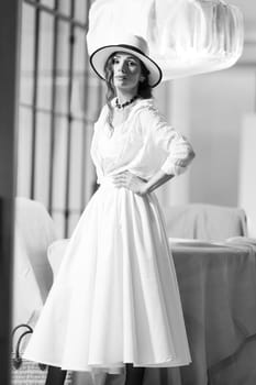 Elegant fashionable woman wearing summer white dress, straw hat, posing in stylish boho interior. Copy, empty space for text