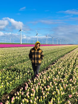 A women is standing amidst a vibrant field of colorful tulips, surrounded by the beauty of nature in full bloom during spring in the Netherlands. woman with windmill turbines