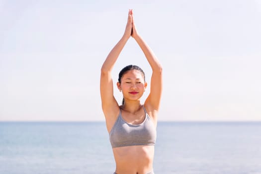 portrait of a young asian woman in sportswear doing yoga position at beach, concept of mental relaxation and healthy lifestyle