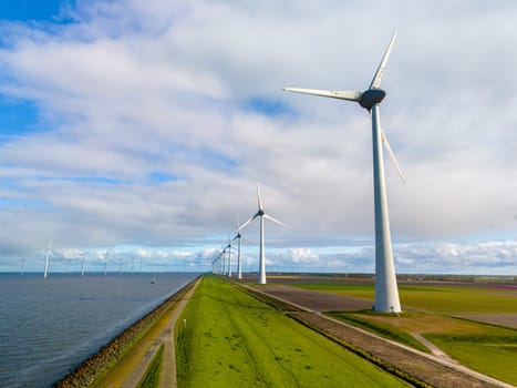 A picturesque scene of sleek wind turbines standing tall in a row next to the ocean on a Dutch dike in Spring, harnessing renewable energy on a bright Spring day. in the Noordoostpolder Netherlands