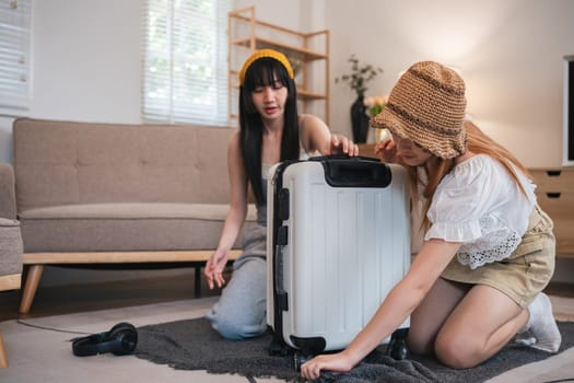 Two young female friends pack a suitcase with clothes and travel passports in preparation for a weekend away..