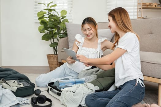 Two young female friends have fun packing supplies and clothes and discussing plans for a vacation together..