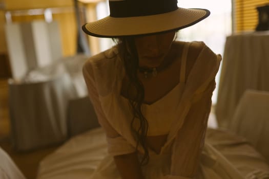 Elegant fashionable woman wearing summer white dress, straw hat, posing in stylish boho interior. Copy, empty space for text