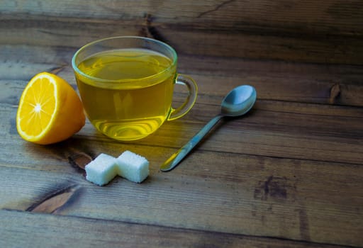 Green tea in a mug, lemon, sugar and a spoon. Green tea in a mug, lemon, sugar and a spoon on a wooden table.