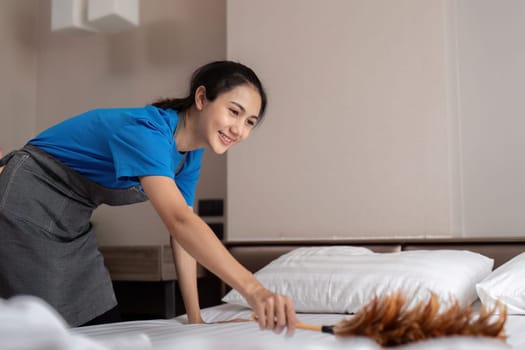 A woman asian staff cleaning service, tool and bucket for work. a young female cleaner with products to clean a bedroom, Dust off the bed.