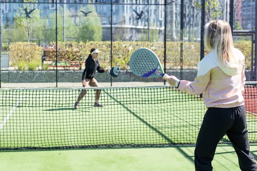 positive mother and daughter standing on court with padel rackets. High quality photo